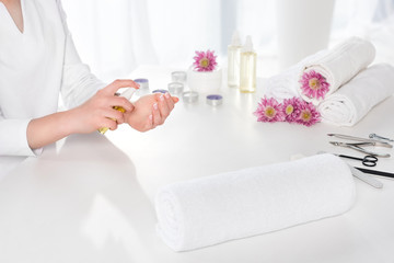 Obraz na płótnie Canvas cropped image of woman using aroma oil at table with towels, flowers, candles and instruments for manicure in beauty salon