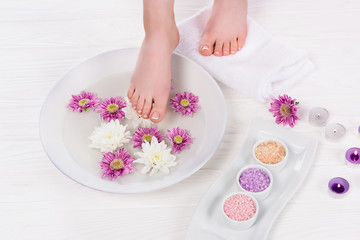 Fototapeta na wymiar cropped shot of barefoot woman receiving bath for nails with colorful sea salt and flowers near aroma candles in beauty salon