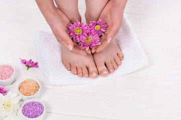 cropped shot of barefoot woman holding flowers near colorful sea salt in beauty salon