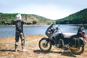 Fototapeta na wymiar motorcycle driver stands with his arms outstretched. for a meeting of adventures on the dirt beach mountain river, enduro, off road, beautiful view, travel equipment, dual sport, space for text