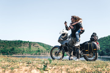 Young romantic couple having fun by the river a off road tourist motorcycle. Love, freedom, togetherness concept. Happy guy and girl travel on a motorbike, enduro touring