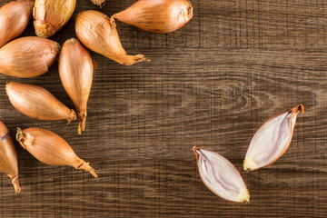 Long golden shallots one cut in two halves flatlay isolated on brown wood background.