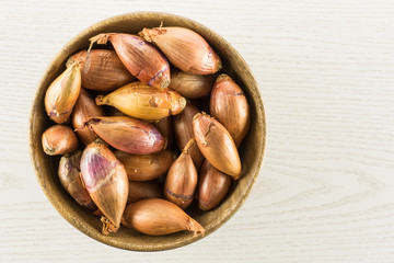 Long shallot in a wooden bowl top view isolated on grey wood background.