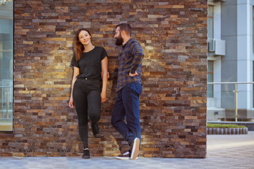 Fototapeta na wymiar Stylish young couple is spending time together outdoors. Attractive woman and handsome bearded man are posing on brick background.