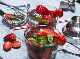 Summer cold drink with strawberries, mint and ice in glass on blue wooden background.