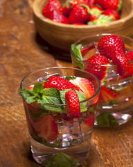 Summer cold drink with strawberries, mint and ice in glass on wooden background. Closeup of cocktails with fresh fruits.