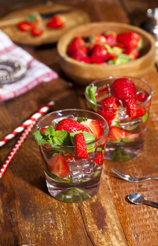 Summer cold drink with strawberries, mint and ice in glass on wooden background. Closeup of cocktails with fresh fruits.