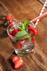 Summer cold drink with strawberries, mint and ice in glass on wooden background. Closeup of cocktails with fresh fruits.