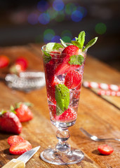 Summer cold drink with strawberries, mint and ice on wooden bar counter . Closeup of cocktail with fresh fruits.