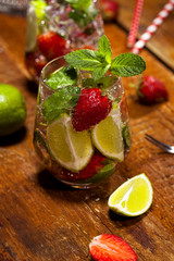 Summer cold drink with strawberries, mint, lime and ice on wooden bar counter . Closeup of cocktail with fresh fruits.