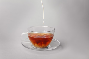 Pouring milk into glass cup with aromatic tea on light background