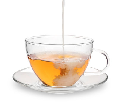Pouring milk into glass cup with aromatic tea on white background