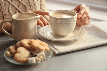 Woman holding cup of aromatic tea with milk at table
