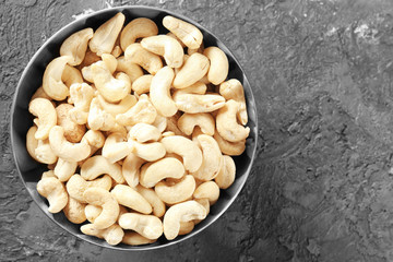 Metal bowl with fresh cashew nuts on grey textured background