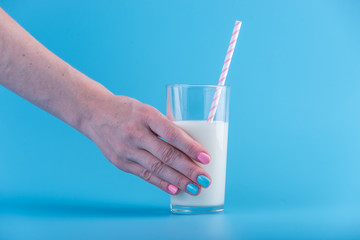 Woman's hand holds glass of fresh milk with a straw on a blue background. Concept of healthy dairy products with calcium