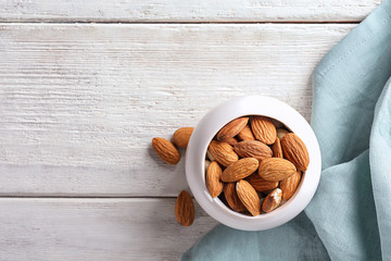 Bowl with fresh almonds on white wooden table