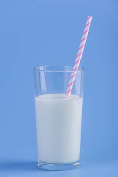 Glass of fresh milk with straw on a blue background. Colorful minimalism. Concept of healthy dairy products with calcium