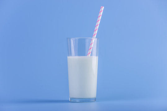Glass of fresh milk with straw on a blue background. Colorful minimalism. Concept of healthy dairy products with calcium