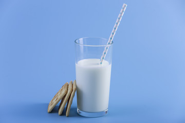 Glass of fresh cow milk with a straw and cookies on a blue background. Concept of healthy dairy products with calcium