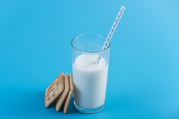 Glass of fresh cow milk with a straw and cookies on a blue background. Concept of healthy dairy products with calcium