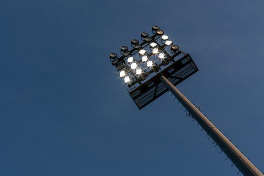 Flutlichtmast mit einigen eingeschalteten Lampen vor dunkelblauem Himmel