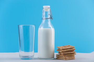 Glass bottle of fresh milk and cookies on blue background. Colorful minimalism. Concept of healthy dairy products
