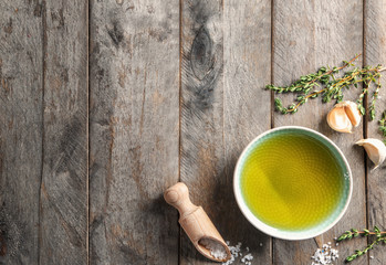 Bowl of olive oil, garlic and scoop with salt on wooden background, top view