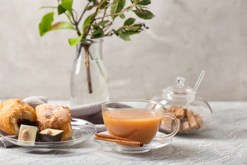 Cup of hot masala tea, cinnamon sticks and treats on wooden table