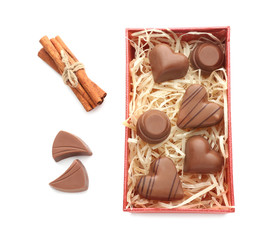 Box with tasty chocolate candies and cinnamon sticks on white background