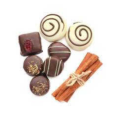 Tasty chocolate candies and cinnamon sticks on white background