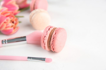 Tasty macarons and makeup brushes on light background