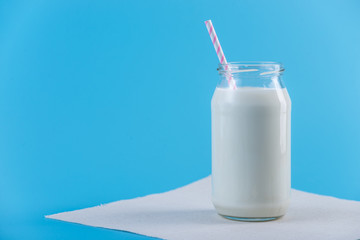 Glass bottle of fresh milk with straw on blue background. Colorful minimalism. Healthy dairy...