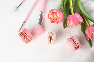 Flat lay composition with tasty macarons, tulips and makeup brushes on light background