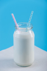 Glass bottle of fresh milk with two straws on blue background. Colorful minimalism. Healthy dairy products with calcium