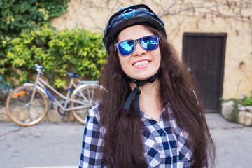 Happy woman with helmet and sunglasses posing backgound bicycle and street
