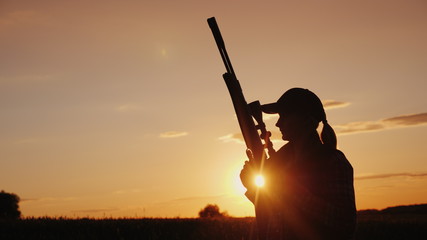 Beautiful silhouette of a woman with a rifle in the rays of the setting sun. Sports shooting and...