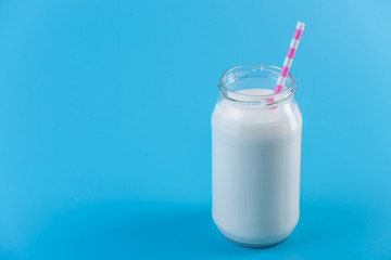 Glass bottle of fresh milk with straw on blue background. Healthy dairy products with calcium