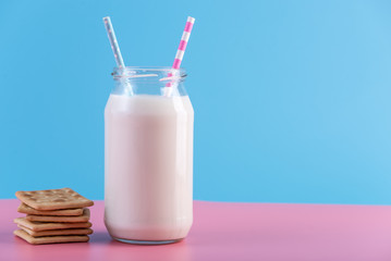 Glass bottle of fresh milk with two straw and cookies on pastel background. Healthy dairy products with calcium