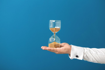 Man holding hourglass on color background. Time management concept