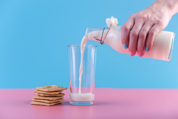 Woman's hand pours fresh milk from bottle into a glass and cookies on a pastel background. Healthy dairy products