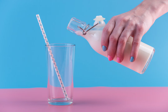 Woman's hand pours fresh milk from bottle into a glass on a pastel background. Concept of healthy dairy products