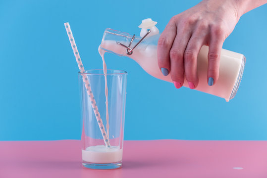 Woman's hand pours fresh milk from bottle into a glass on a pastel background. Concept of healthy dairy products