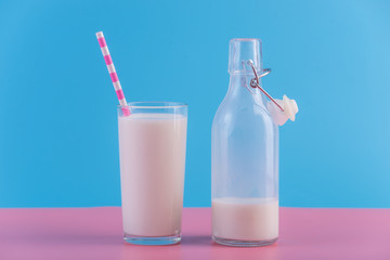 Bottle of fresh milk and a glass with a straw on a pastel background. Colorful minimalism. Healthy dairy products
