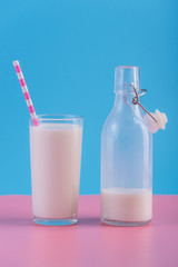 Bottle of fresh milk and a glass with a straw on a pastel background. Colorful minimalism. Healthy dairy products