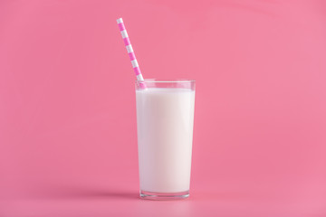 Glass of fresh milk with a straw on a pink background. Colorful minimalism. Healthy dairy products with calcium