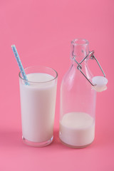 Glass bottle of fresh milk and a glass with a straw on a pink background. Healthy dairy products with calcium