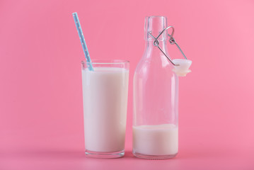 Glass bottle of fresh milk and a glass with a straw on a pink background. Healthy dairy products with calcium
