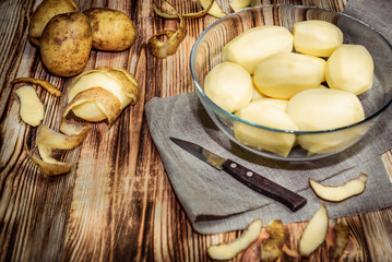 Raw peeled sliced potato, pile of potatoes and knife on rustic wooden table.