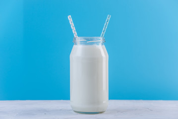 Glass bottle of fresh milk with two straws on blue background. Colorful minimalism. Healthy dairy products