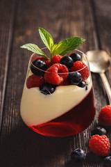 Pannacotta with berry jelly and berries on dark background.